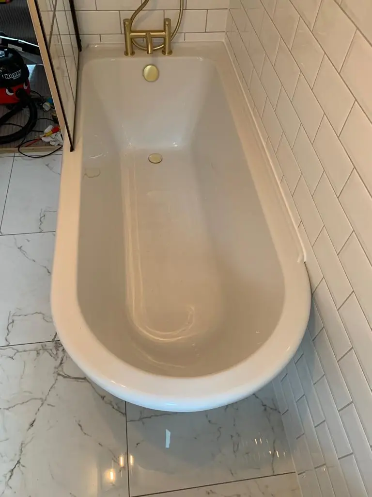 White bath with brass bath shower mixer, white metro walls and marble-effect floor tiles