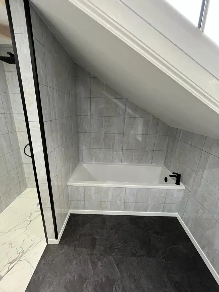 Bath fitted under the sloped eaves with matt black mixer tap and grey stone-effect tiles