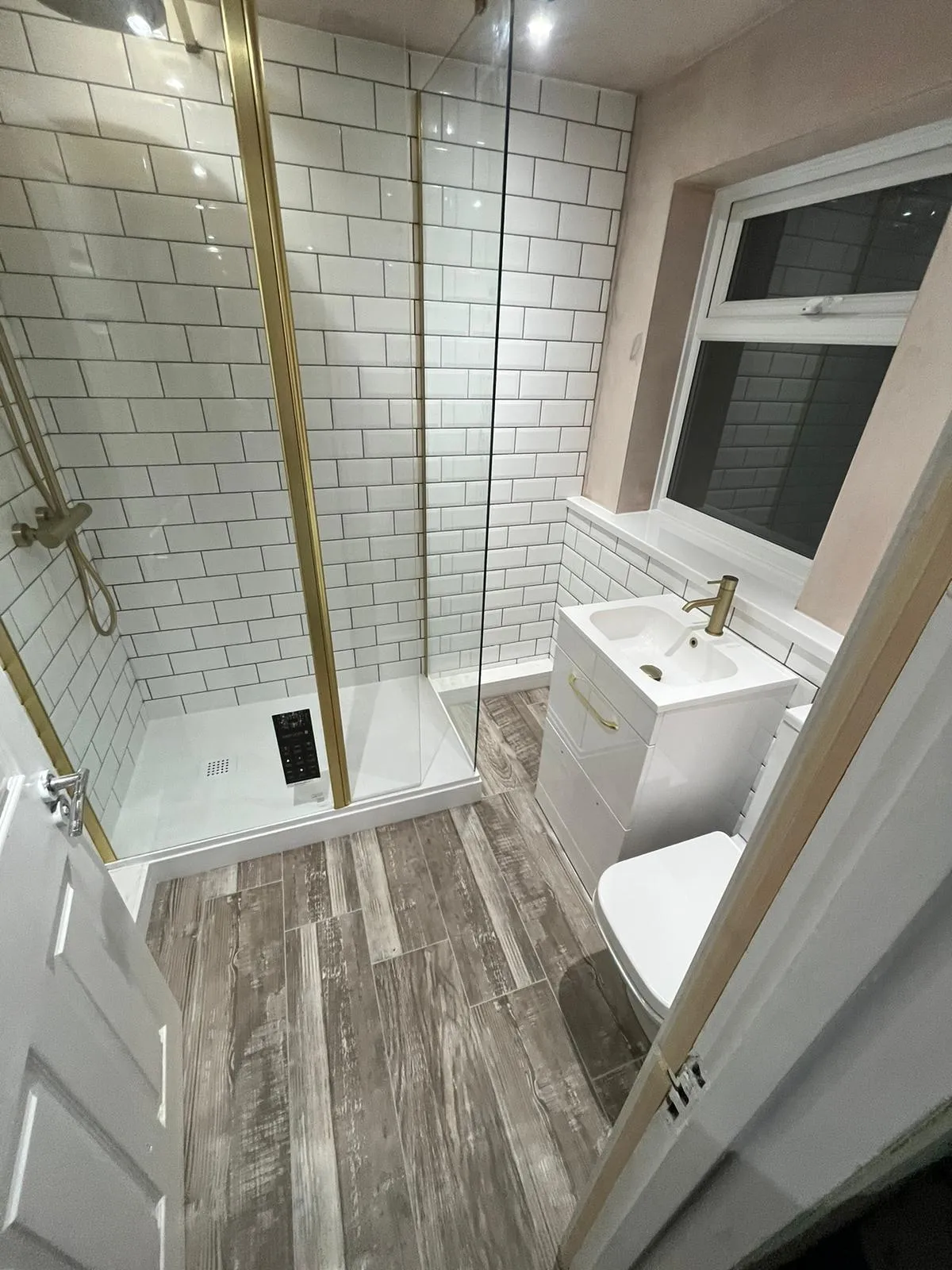 Brass-framed walk-in shower with white metro tiles and rustic wood-effect floor