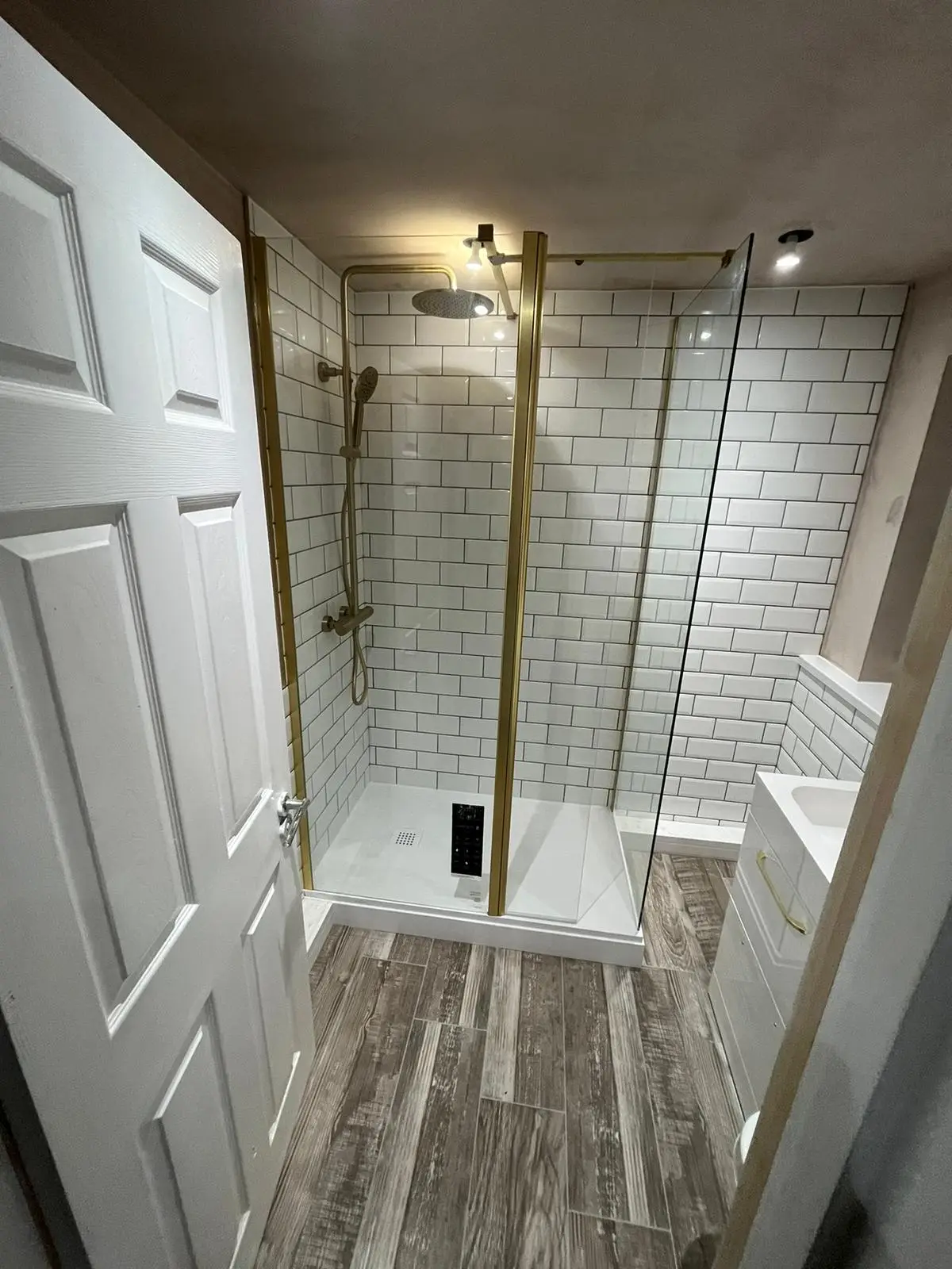 Brass rainfall shower column inside a metro-tiled walk-in enclosure