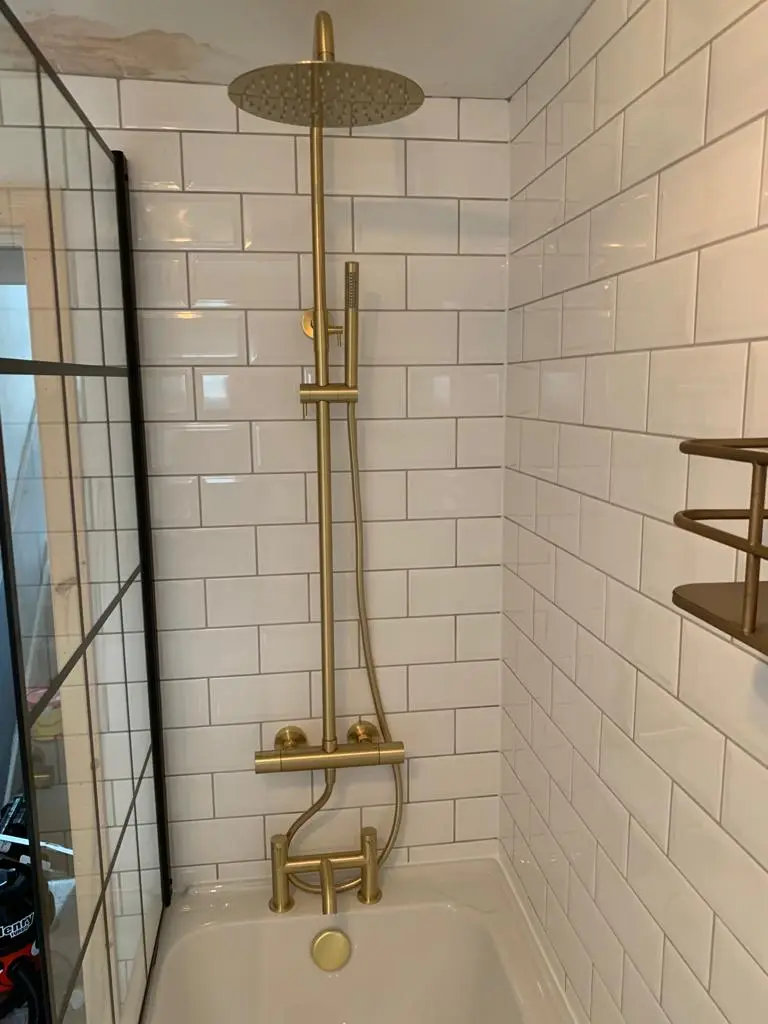 Brushed brass thermostatic shower column over the bath against white bevelled metro tiles