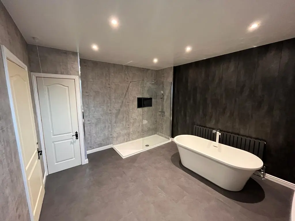 Master bathroom with freestanding bath against a charcoal feature wall and large walk-in shower