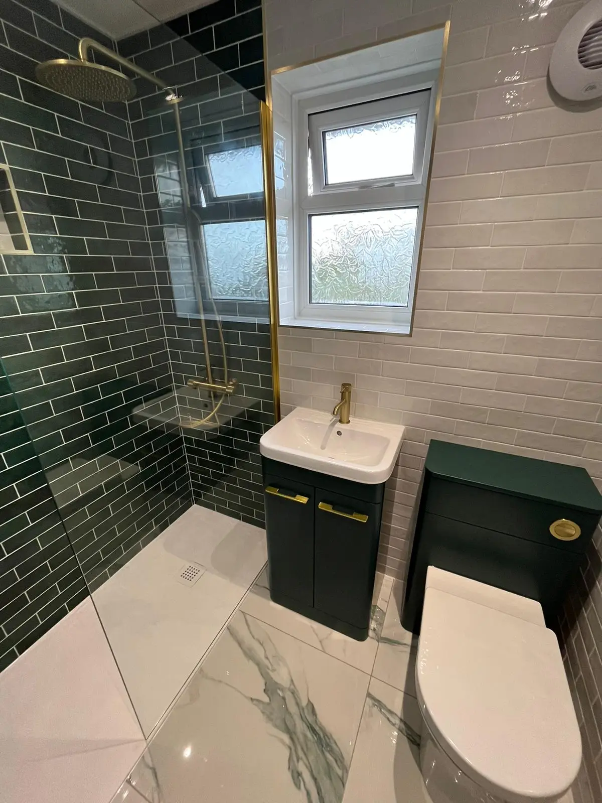 Walk-in shower with emerald green metro tiles, brushed brass rainfall head and brass-trimmed glass screen