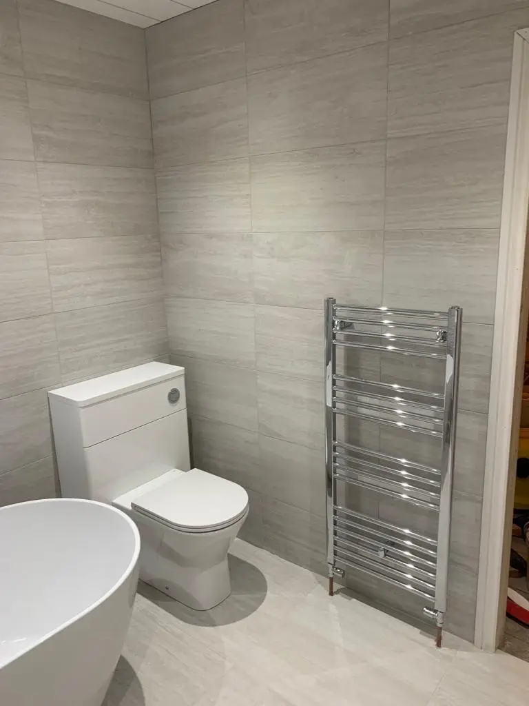 Freestanding bath beside a chrome towel radiator on stone-effect tiles