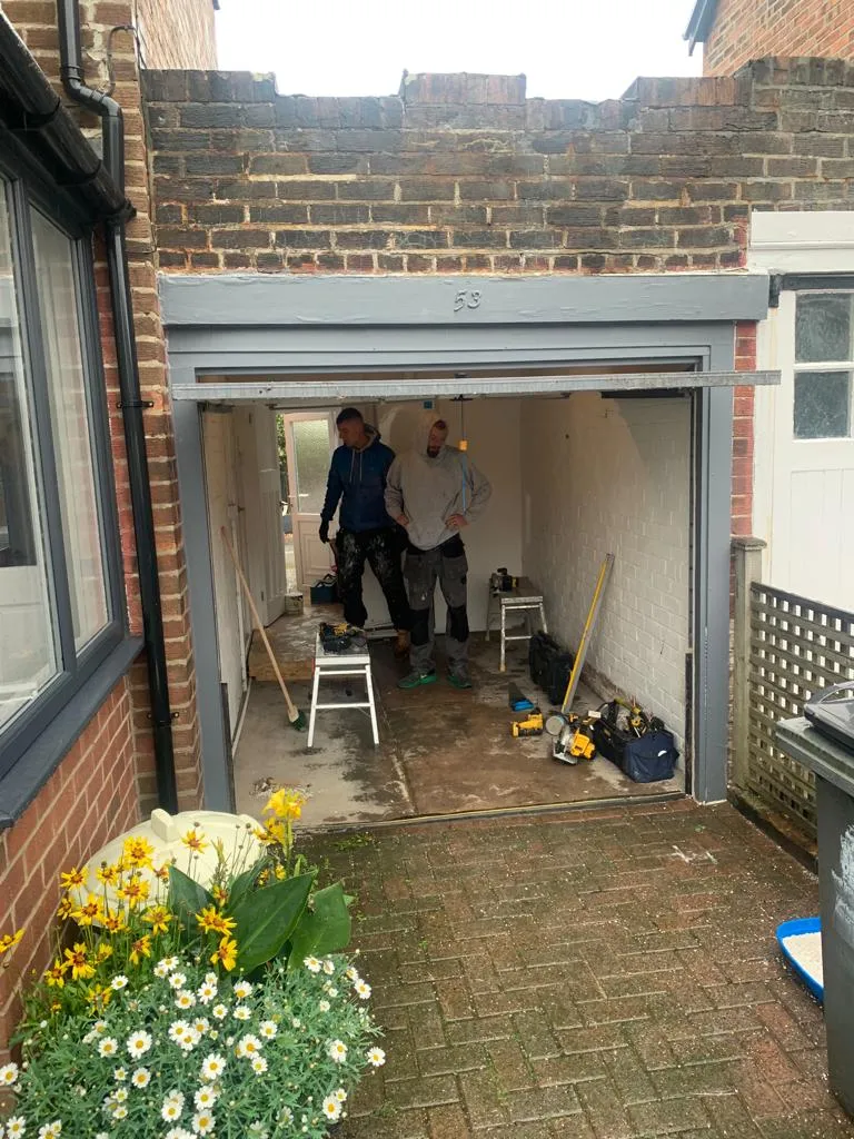 Two tradesmen working inside a garage mid-conversion, roller door removed