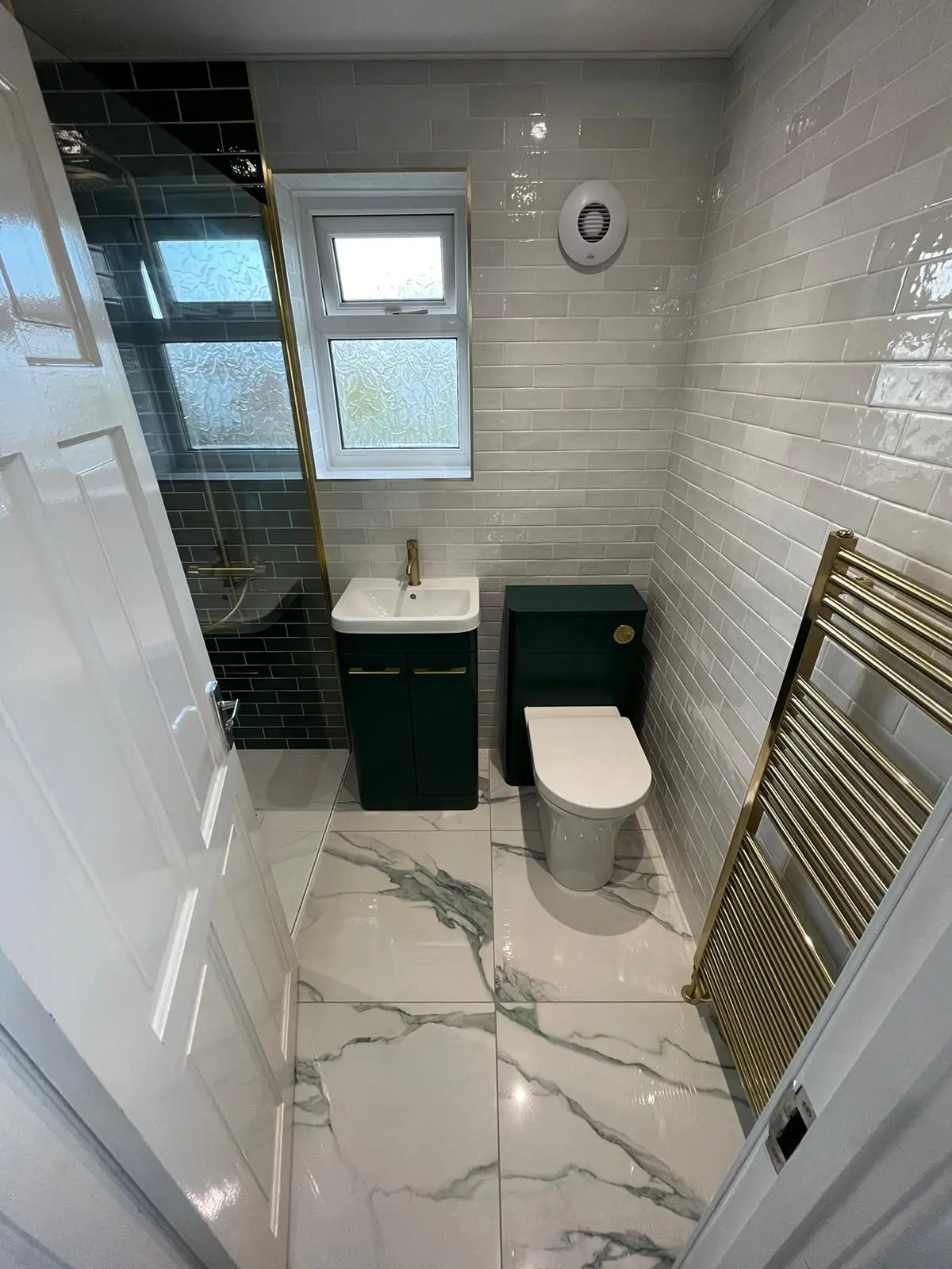 Forest green vanity and WC unit with brass handles, brass towel radiator and marble-effect porcelain floor