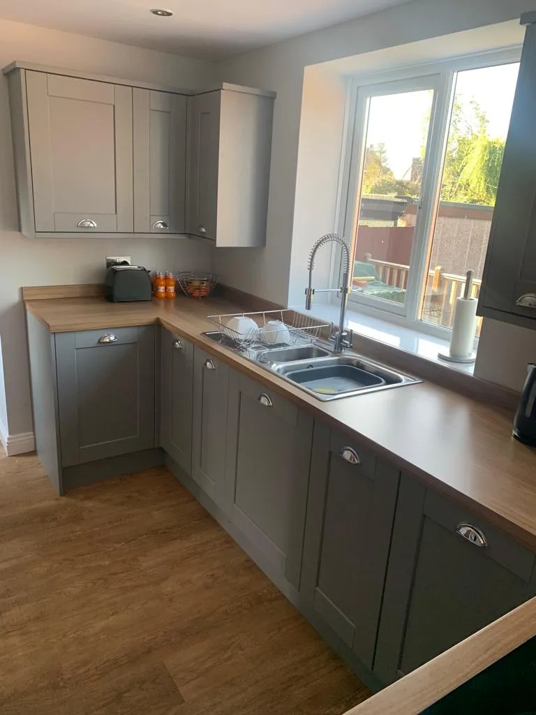 Grey shaker kitchen run under a sunny window with pull-out mixer tap and garden view