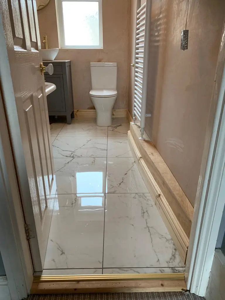 Marble-effect porcelain floor with gold trim at the threshold, grey vanity and white towel radiator