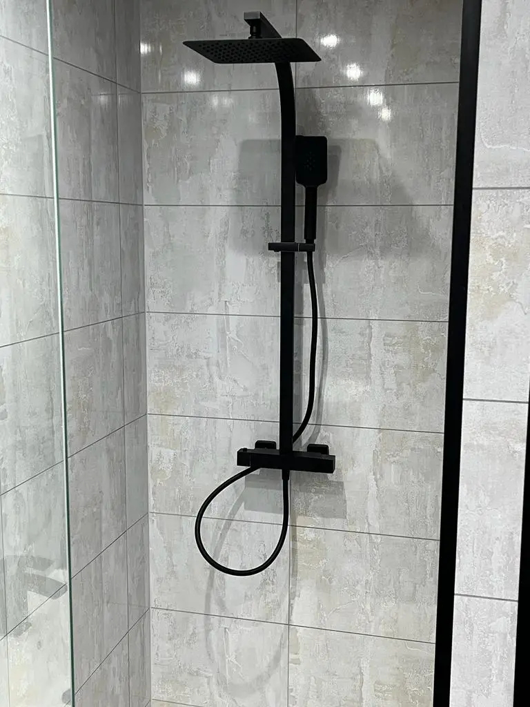 Matt black thermostatic shower column against soft grey stone-effect tiles