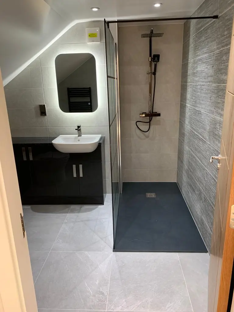 Loft en-suite with matt black shower kit, black slate-effect tray and backlit mirror under the sloped ceiling