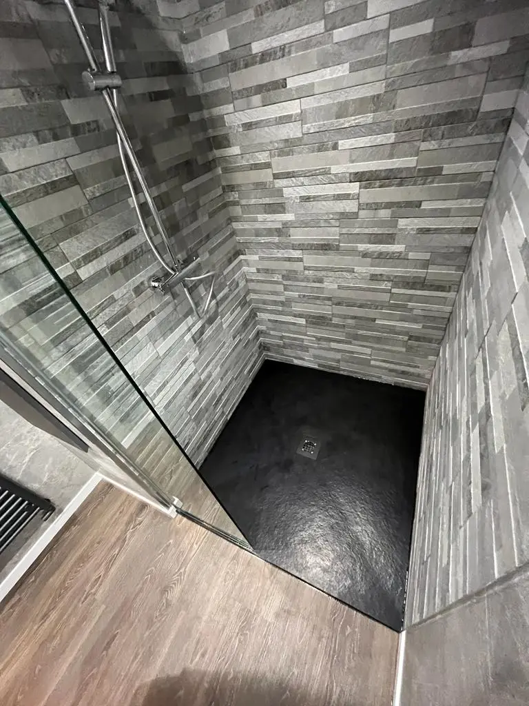 Walk-in shower lined with grey split-face stone tiles over a black slate-effect tray